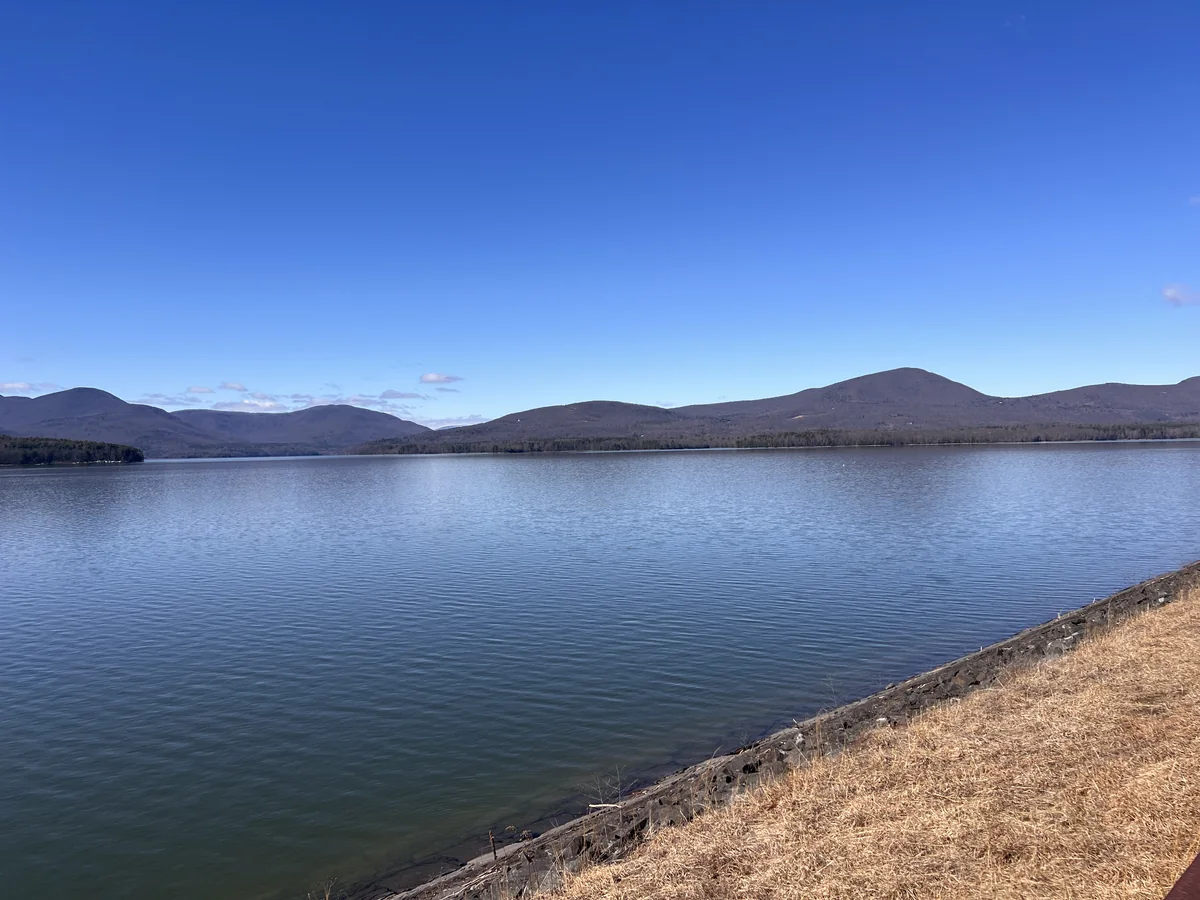 The Ashokan Reservoir under a clear blue sky, with low Catskill mountains across the water and dry grass on the stone shoreline