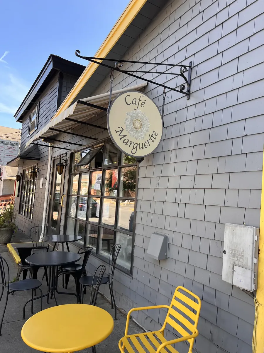 Round Cafe Marguerite sign over a shingled storefront with yellow tables and chairs on the sidewalk in Margaretville, NY