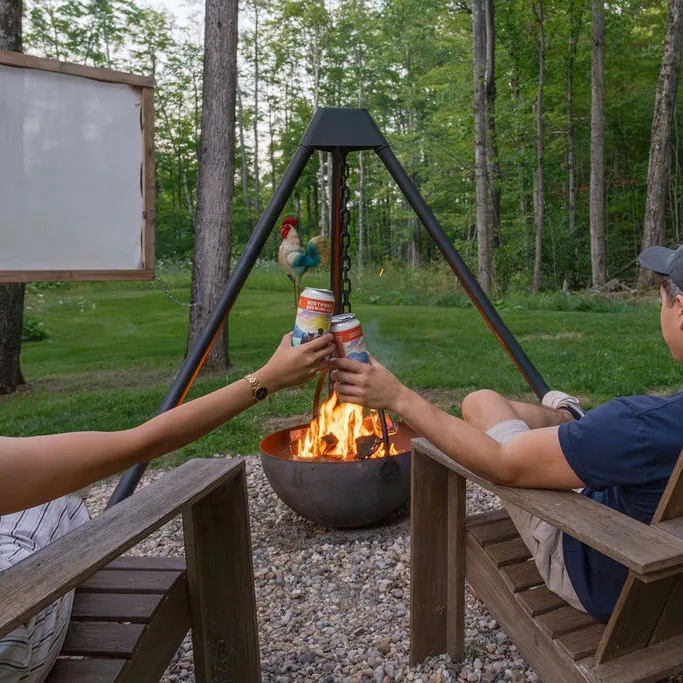 Two friends in Adirondack chairs toasting beside a fire pit at a cabin in the woods