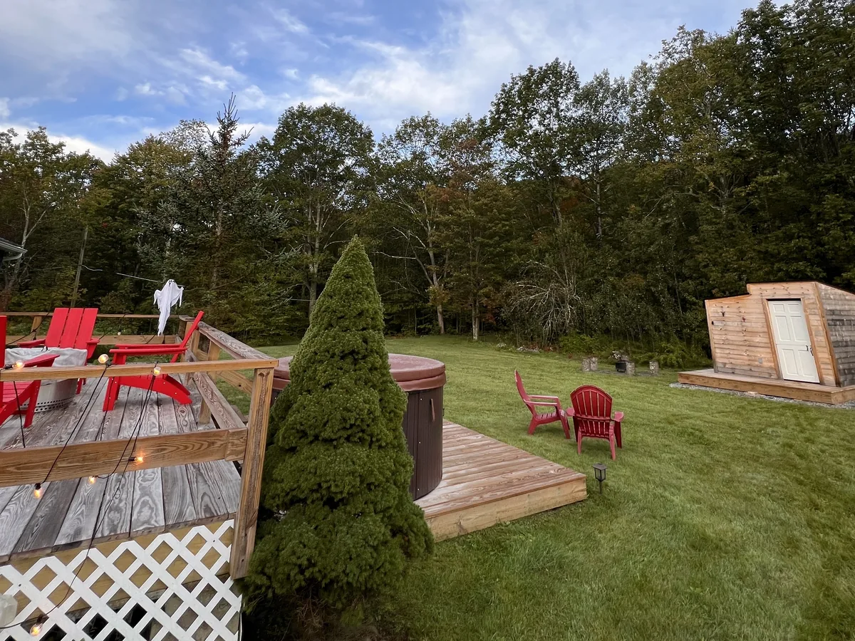 Clove Creek Cabin deck with red Adirondack chairs, a hot tub and a cedar sauna on the lawn in Hunter, NY