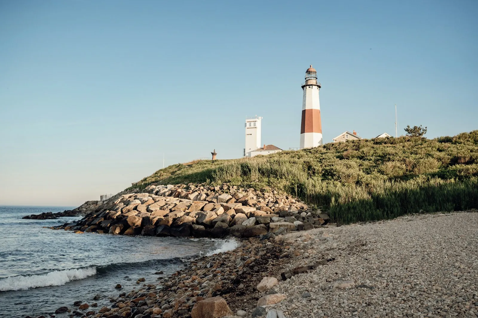 Montauk Point Lighthouse on a grassy bluff above a rocky beach and the Atlantic at the eastern tip of Long Island