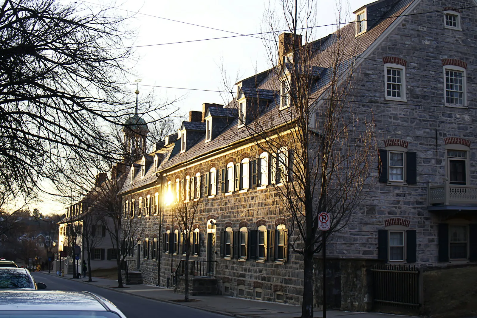 Sunset light on a row of old stone buildings with dormer windows and a cupola along a street in historic Bethlehem, Pennsylvania