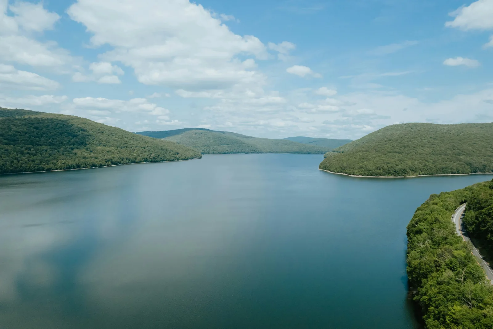 The Pepacton Reservoir stretching between green wooded hills under a partly cloudy sky near Downsville, NY